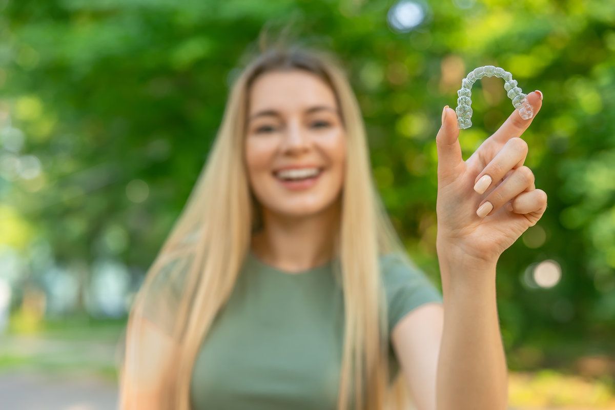 Happy girl in green t-shirt holding removable braces or aligners for straightening and whitening teeth on green background